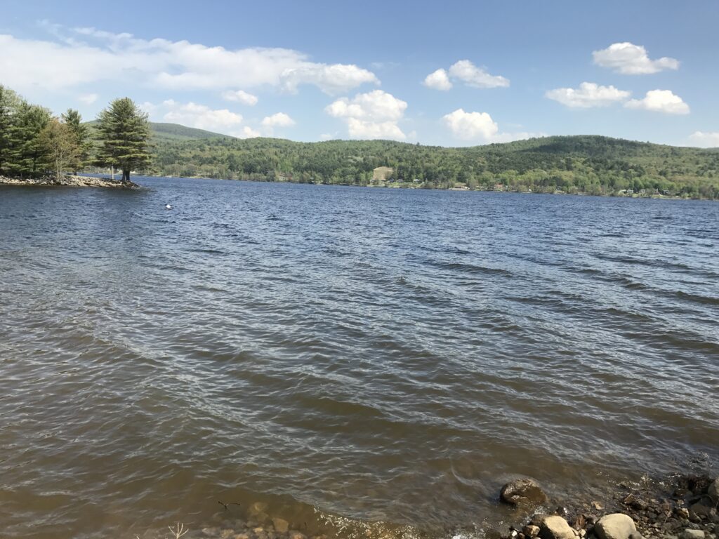 Great Sacandaga Lake with rippled water, a rocky foreground, and wooded hills along the opposite shore.