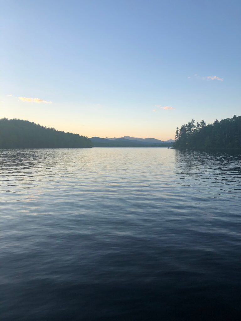 Evening light over Schroon Lake, with rippled water, wooded shores, and distant mountain ridges.
