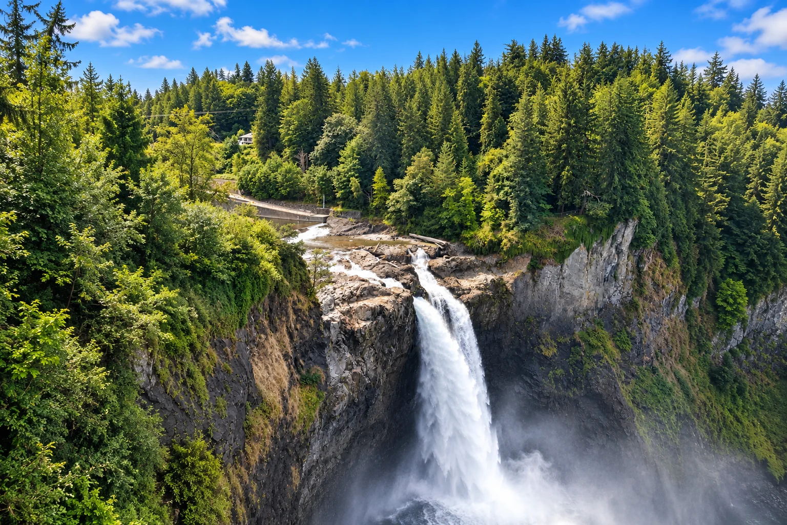 Snoqualmie Falls cascading between rocky cliffs and evergreen forest beneath a bright blue sky.
